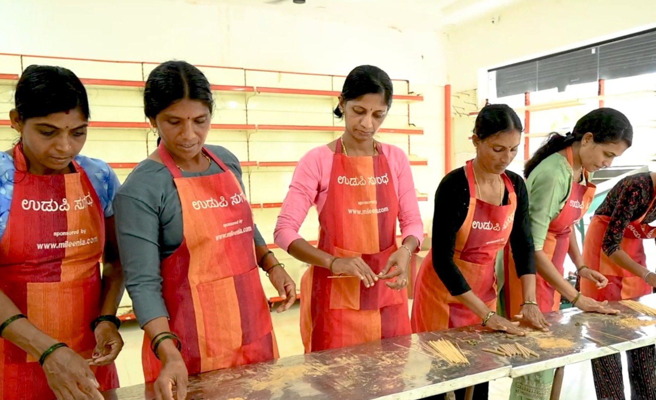 Women in Udupi Sugandha aprons hand-rolling incense sticks at a long table in the Navunda facility